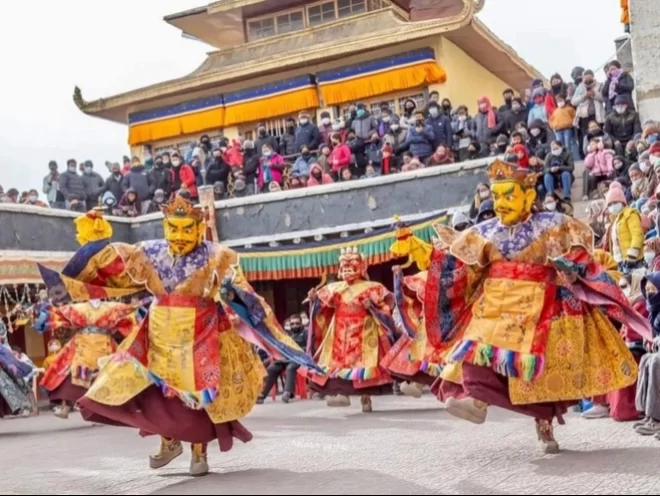 Masked monks performing cham dance at Spituk Gustor Festival in Ladakh, featuring colourful silk robes and monastery crowd, perfect Ladakh cultural tour package