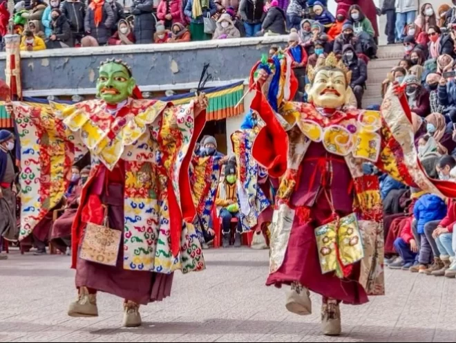 Masked monks in cham dance at Spituk Gustor Festival in Ladakh, featuring colourful robes and monastery crowd, perfect Ladakh cultural tour package