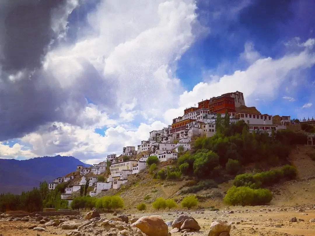 Thiksey Gompa rising on hill in Ladakh during partly cloudy day, featuring white stupas and distant mountains, perfect Ladakh tour package.
