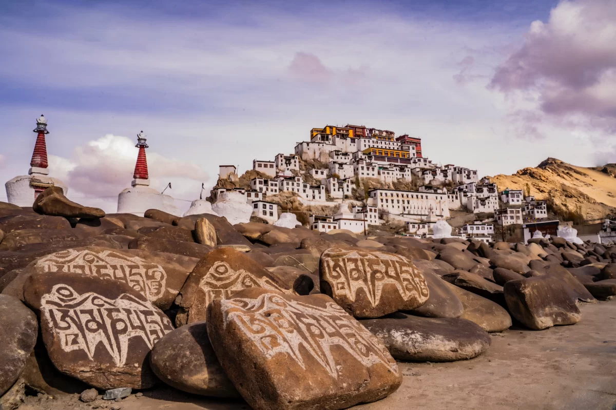 Thiksey Gompa against dramatic clouds in Ladakh, featuring chortens, mani stones and hilltop buildings, perfect Ladakh tour package