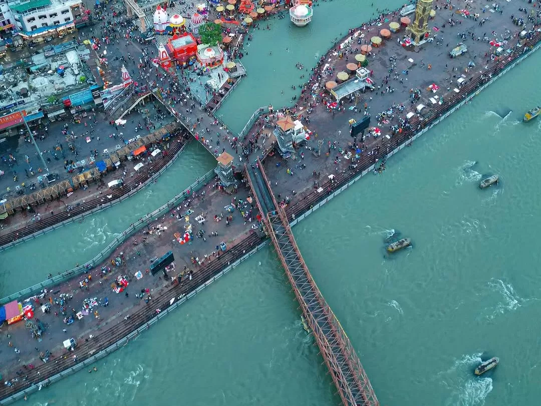 Har Ki Pauri Haridwar aerial top-down view of crowded Ganga ghats festival tents boats colorful stalls iron bridge during Kumbh Mela, perfect pilgrimage panorama, Uttarakhand tour packages.