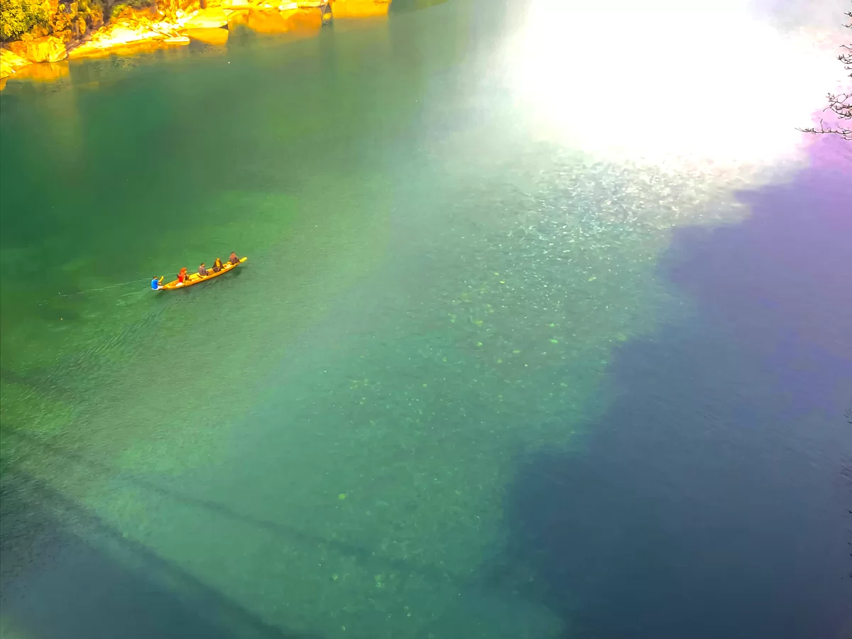 Umngot River Dawki Meghalaya aerial view crystal clear emerald green waters wooden boat tourists golden sunlight riverbanks serene peaceful vibe perfect boating adventure Meghalaya tour package.