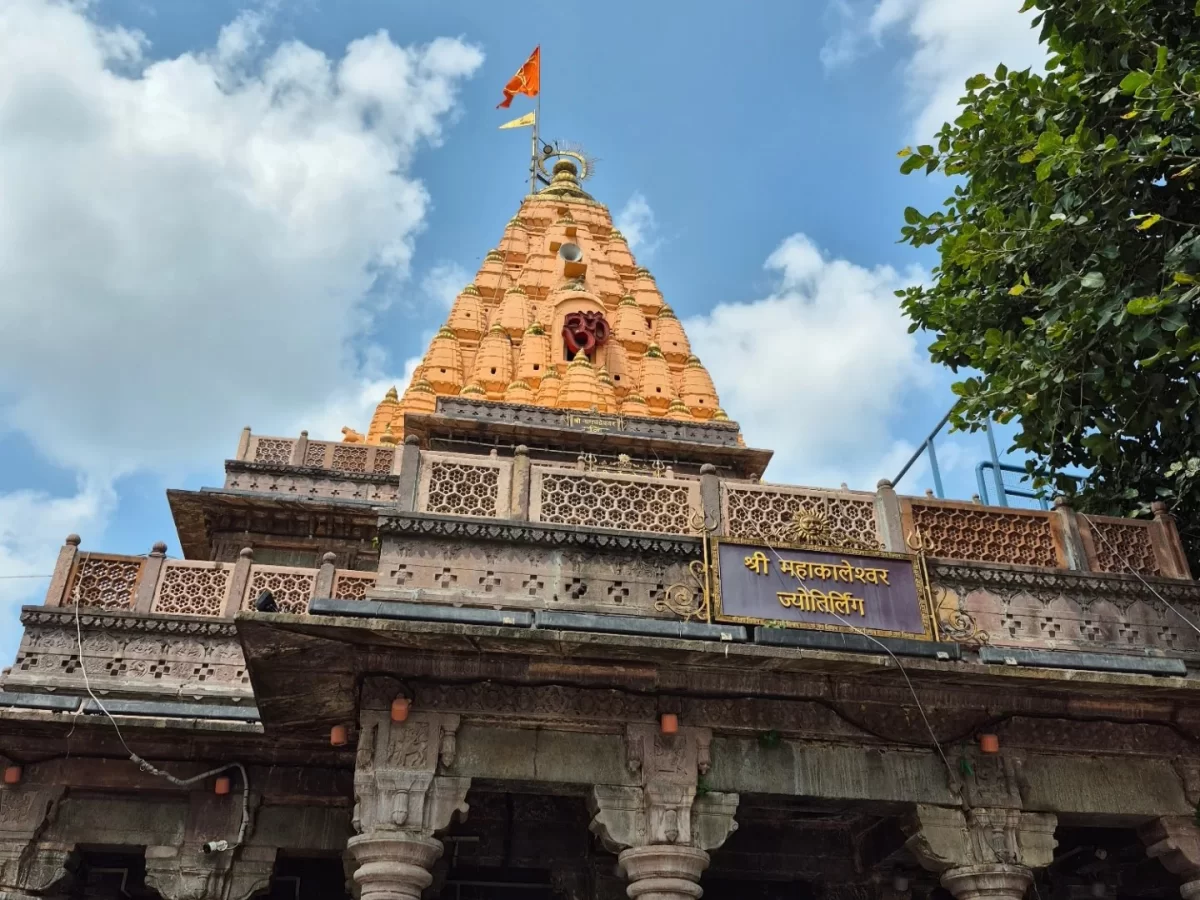 Shree Mahakaleshwar Temple entrance at Ujjain during clear daylight, featuring pink stone pillars arches yellow banner trees, perfect spiritual Madhya Pradesh tour package.