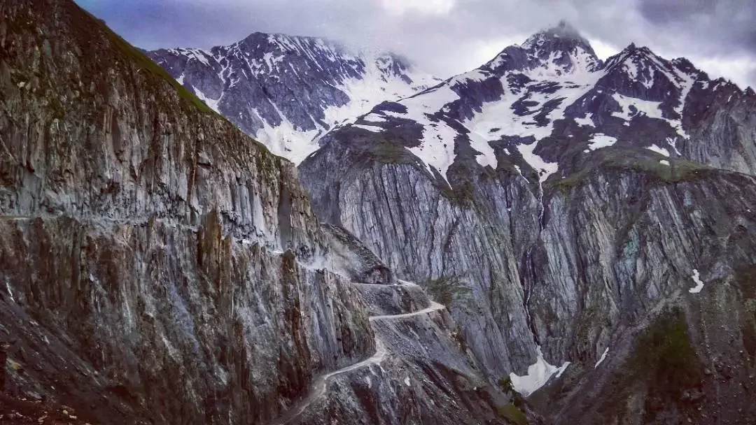 Zoji La Pass Ladakh dramatic overcast view of treacherous mountain road snaking through snow-capped Himalayan peaks on Srinagar-Leh National Highway, highest motorable pass adventure in Ladakh tour pa