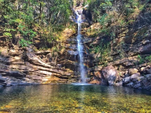 Bhalu Gaad Waterfall Mukteshwar sunny cascade over terraced rocks framed by dense trees into clear pool, perfect scenic trek destination, Uttarakhand tour packages.