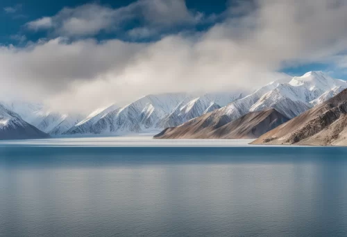 Stylized Leh–Ladakh milestone reading 0 km with snow-covered mountain peaks and colorful prayer flags, explore winter ladakh package