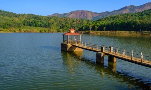 Hirekolale Lake in Chikkamagaluru during daylight, featuring serene lake, mountain views and lakeside pavilion, perfect nature experience, Karnataka tour packages.
