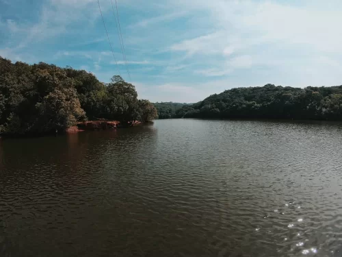 Charlotte Lake at Matheran during partly cloudy skies, featuring lush forested banks and calm water ripples, perfect romantic experience Maharashtra tour package.
