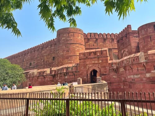 Agra Fort Uttar Pradesh red sandstone walls curved bastions arched entrance tourists trees railings blue sky Yamuna River view UNESCO heritage, perfect Golden Triangle heritage package.