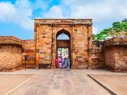 Taragarh Fort Ajmer grand yellow sandstone gateway with massive arched entrance flanked by bastions against Aravalli hill backdrop tourists walking pathway historic fortress in Rajasthan tour packages