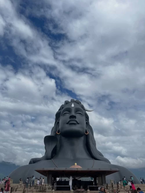 Iconic Adiyogi Shiva statue with visitors at the base in Coimbatore, Tamil Nadu, set against a dramatic cloudy sky, a spiritual attraction featured in Tamil Nadu tour packages.