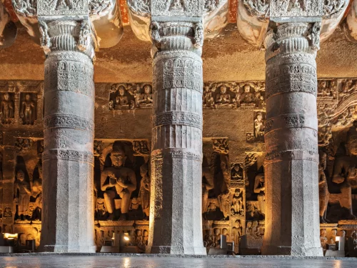 Ajanta Caves Maharashtra UNESCO ancient rock-cut Buddhist cave interior showcasing ornate intricately carved stone pillars Buddha statues illuminated dramatically, must-visit heritage tour package.
