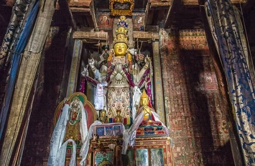 Buddha statue at Alchi Gompa Ladakh in dimly lit shrine during misty weather, featuring multiple arms prayer scarves and wall murals, perfect spiritual Ladakh tour package.