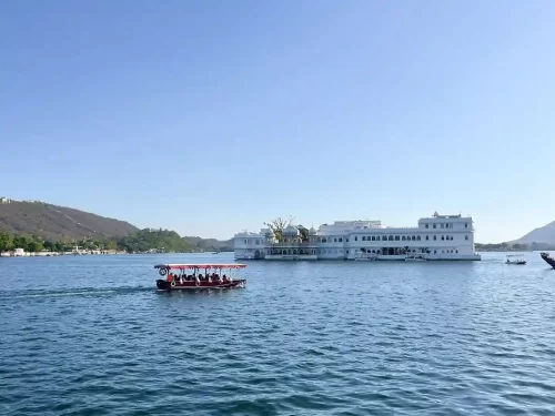 Ambrai Ghat view of Lake Pichola with a tourist boat and Taj Lake Palace, a top sightseeing spot in Udaipur.