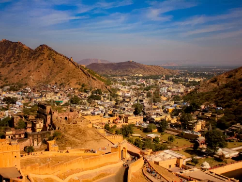 Panoramic aerial view of Amer Fort (Amber Fort) in Jaipur Rajasthan overlooking Maota Lake, colorful old town, Aravalli hills under golden sunset sky, perfect Rajasthan tour package.