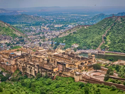 Aerial view of City Palace in Udaipur Rajasthan with lakeside palaces, courtyards, Jag Mandir island and surrounding Aravalli hills under misty sky, perfect Rajasthan tour package.