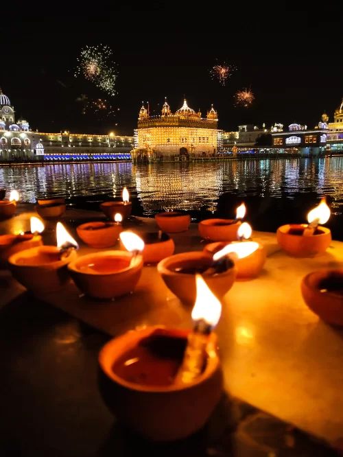 Golden Temple illuminated at night in Amritsar, Punjab, with diyas glowing in the foreground and fireworks in the sky, a sacred Sikh pilgrimage site featured in Punjab tour packages.
