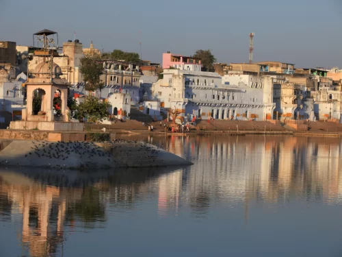 Whitewashed havelis temples and ghats along Pushkar Lake Rajasthan at golden hour with serene reflective waters pigeons and vibrant sky, iconic spiritual cultural Rajasthan tour package destination 