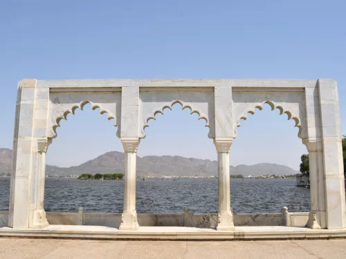 Marble pavilion arches framing Fateh Sagar Lake Udaipur Rajasthan with distant Aravalli hills blue waters and clear skies, iconic romantic heritage Rajasthan tour package viewpoint.