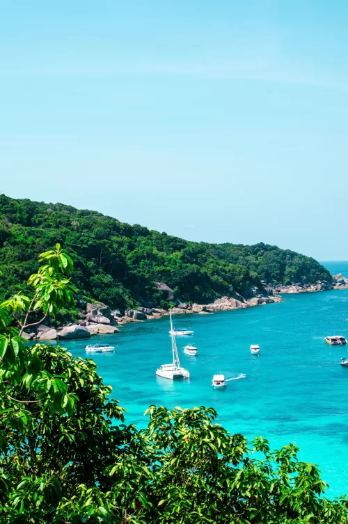 Crystal clear turquoise waters with anchored boats and lush green coastline in Andaman highlighting serene island scenery ideal for Andaman island tour packages
