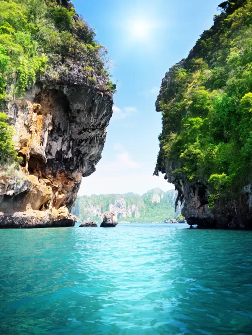 Turquoise waters flowing between towering limestone cliffs covered in lush greenery in Andaman, a breathtaking island landscape often explored through Andaman tour packages.