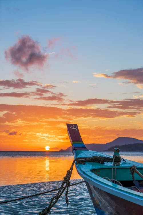 Golden sunset over tranquil sea in Andaman with colorful wooden boat anchored near shore creating a peaceful tropical escape perfect for Andaman island tour packages