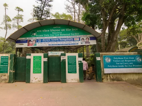 Main entrance gate at Assam State Zoo cum Botanical Garden Guwahati during cloudy day, featuring welcome sign trees bamboo fence, perfect family experience Assam tour package.