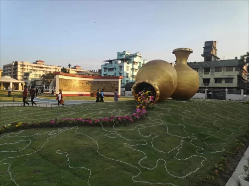 Giant golden flower pot sculptures at Atal Udyan Adabari Park Guwahati during sunset, featuring colorful flowers green lawns, perfect family experience Assam tour package. 