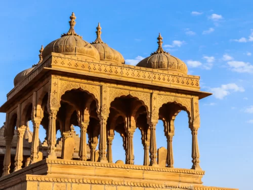 Bada Bagh Jaisalmer majestic yellow sandstone chhatri with triple domes detailed arches pillars blue skies, perfect Rajasthan heritage cultural tour packages. 