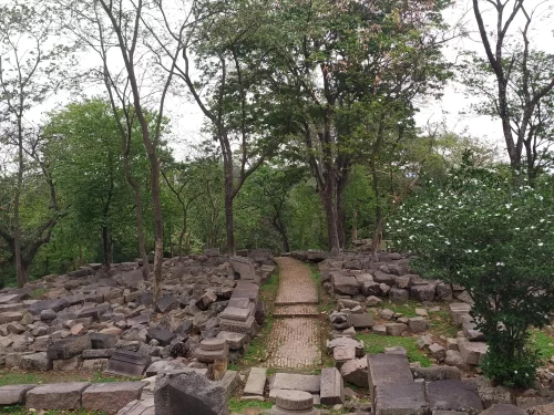 Bamuni Hills Tezpur ancient stone ruins scattered blocks brick pathway trees greenery cloudy sky Chitralekha Udyan park, perfect 9th-10th century archaeological exploration Assam tour packages.