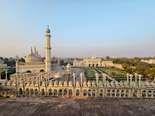 Asafi Mosque and Bara Imambara at Lucknow during sunrise, featuring white domes minarets lawns trees skyline, perfect cultural Uttar Pradesh tour package.