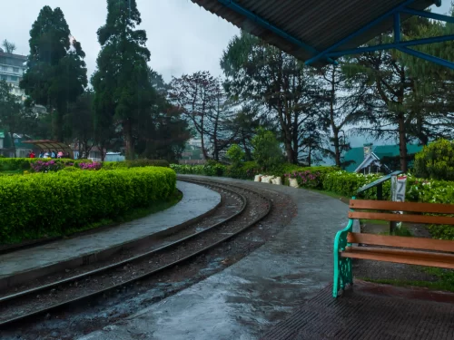 Batasia Loop in Darjeeling during rainy evening, featuring curved toy train tracks, garden walkway and benches, perfect scenic Sikkim tour package