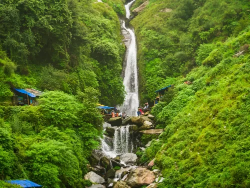 Bhagsu Waterfall pathway at McLeod Ganj Dharamshala during misty monsoon, featuring lush green forests, blue tents, rocks, perfect adventure Himachal Pradesh tour package.
