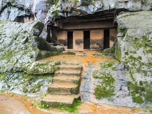 Ancient cave entrance with three doors at Bhaja Buddhist Caves during rainy mist, featuring stone steps mossy rocks, perfect heritage experience Pune caves tour package. 