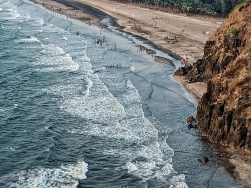 Aerial view of Bhatye Beach in Ratnagiri, Maharashtra, with waves rolling onto the sandy shoreline and rocky cliffs along the coast, a scenic stop featured in Maharashtra tour packages.