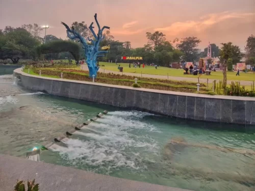  Bhawartal Garden in Indore featuring landscaped lawns, a flowing water channel, and evening visitors under a sunset sky, a popular stop in Madhya Pradesh tour packages