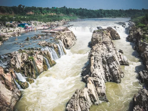 Dhuandhar Falls cascading at Bhedaghat Jabalpur during clear afternoon, featuring Narmada River gushing through marble gorges and tourist platforms, perfect adventure experience in Madhya Pradesh tour package.