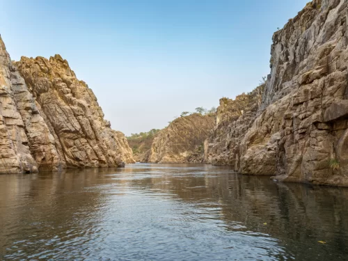Marble Rocks canyon at Bhedaghat Jabalpur during clear afternoon, featuring towering white cliffs and serene Narmada River, perfect adventure experience in Madhya Pradesh tour package.