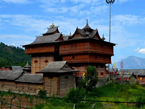 Bhimakali Temple Sarahan during partly cloudy skies, featuring multi-tiered wooden tower prayer flags surrounding structures pine mountains meadows, perfect heritage experience Himachal Pradesh tour package.