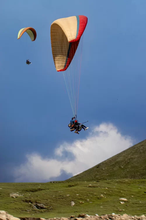 Paragliders soaring over the green hills of Bir Billing, Himachal Pradesh, against a clear blue sky, a popular adventure destination known for paragliding in India.