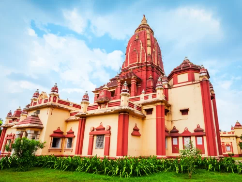 Mathura Birla Mandir Uttar Pradesh Gita Temple red sandstone architecture with golden spires, cream walls, intricate arches, lush green gardens under partly cloudy blue skies, perfect Krishna heritage India tour package.