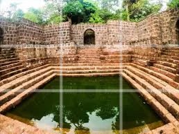 Stepped stone tank of Brahma Kund in Alibaug, Maharashtra, surrounded by historic laterite walls and greenery, a cultural landmark featured in Maharashtra tour packages. 