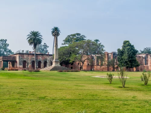 British Residency pillar ruins at Lucknow during clear day, featuring red brick arches palms trees lawns, perfect heritage Uttar Pradesh tour package.