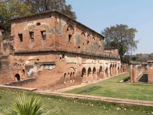 British Residency ruins at Lucknow during sunny day, featuring red brick arches lawns palms trees, perfect heritage Uttar Pradesh tour package.