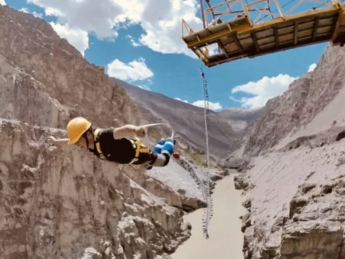 A person bungee jumping from a platform over a canyon river in Leh, Ladakh.