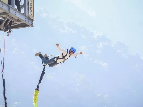 Bunjee Jumping person leaping from a high platform wearing a safety harness and helmet during an adrenaline filled bungee jumping adventure against a scenic mountain backdrop.