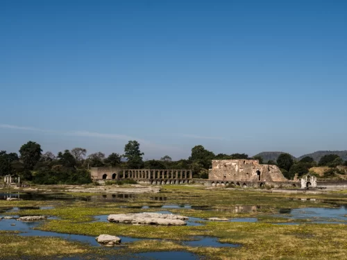 Rani Roopmati Pavilion at Mandu under clear skies, featuring Rewa Kund bridge ruins amid reservoir reflections, perfect heritage experience with Madhya Pradesh tour packages.