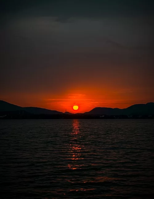 Stunning sunset over Chilika Lake Odisha with glowing orange sky and mountain silhouettes reflecting tranquil beauty in Odisha tour packages