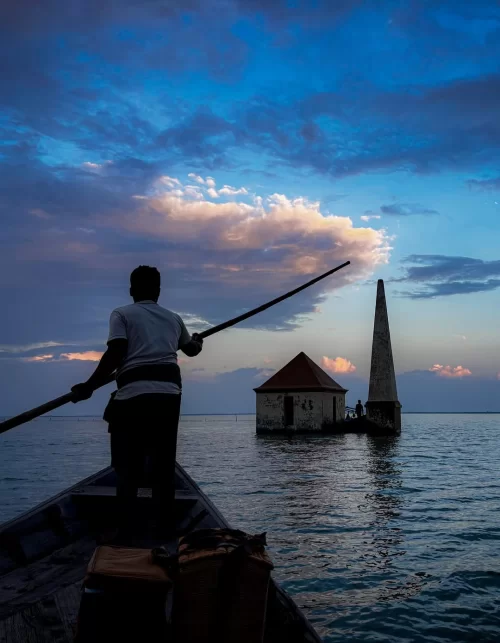 Silhouette of boatman rowing towards temple structure at Chilika Lake Odisha under dramatic evening sky featured in Odisha tour packages