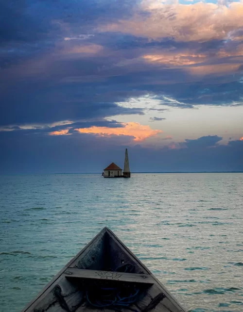 Boat view towards small temple structure at Chilika Lake Odisha during dramatic sunset sky reflecting serene moments in Odisha tour packages